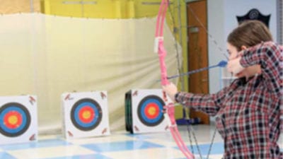 Senior Rachael Jaszczak pulls back her bow, getting ready to take her shot in the cafeteria on Feb. 11 during Archery Club practice. Photo by Creede McClellen.